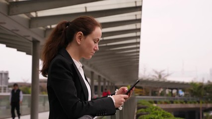 Business woman using smartphone, stay at pedestrian passage over city highway, half length side portrait of professional person. Roofed overpass bridge to Hong Kong pier