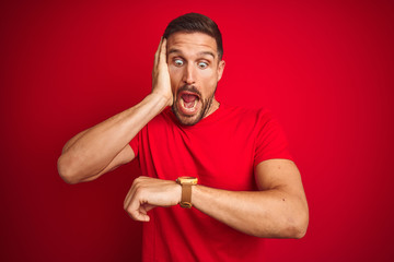 Young handsome man wearing casual t-shirt over red isolated background Looking at the watch time...