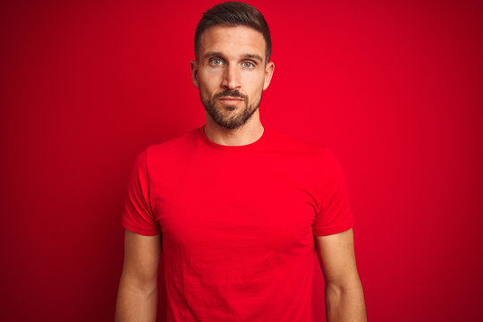 Young handsome man wearing casual t-shirt over red isolated background Relaxed with serious expression on face. Simple and natural looking at the camera.