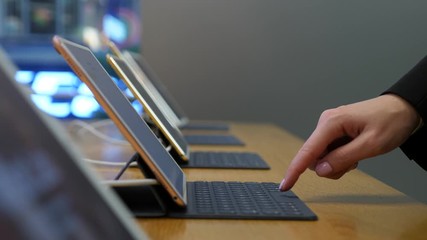Customer woman trying modern tablet at store, use detachable keyboard to type text, press on buttons by one finger then use both hands. Closeup shot, several devices set out for display at desk