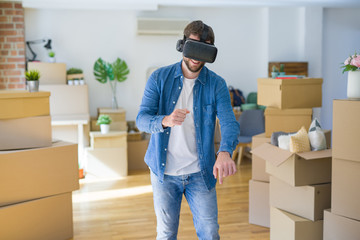 Young man wearing virtual reality glasses playing a simulation game around cardboard boxes moving to a new house