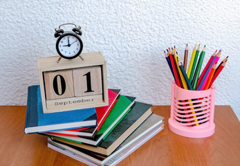 calendar with the date of the first of September and an alarm clock, color pencils on the table