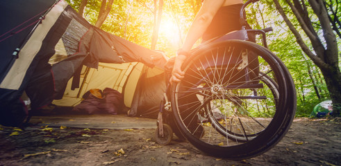 Disabled man resting in a campsite with friends. Wheelchair in the forest on the background of tents