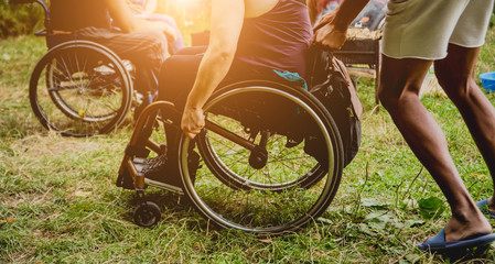 Disabled man resting in a campsite with friends. Wheelchair in the forest on the background of tents