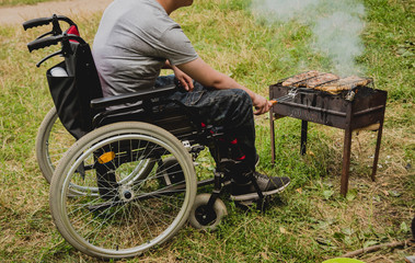 Disabled man resting in a campsite with friends. Wheelchair in the forest on the background of...