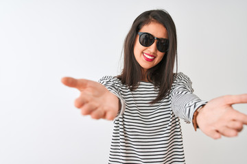 Chinese woman wearing striped t-shirt and sunglasses standing over isolated white background looking at the camera smiling with open arms for hug. Cheerful expression embracing happiness.