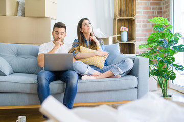 Young beautiful couple relaxing sitting on the sofa of new house using computer laptop serious face...