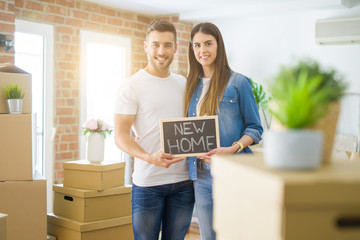 Beautiful young couple moving to a new house, smiling very happy holding blackboard with new home text