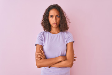 Young brazilian woman wearing t-shirt standing over isolated pink background skeptic and nervous, disapproving expression on face with crossed arms. Negative person.