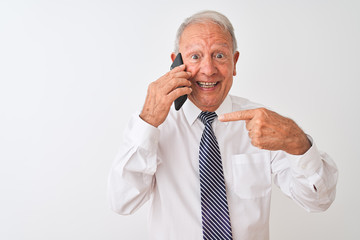 Senior grey-haired businessman talking on the smartphone over isolated white background very happy pointing with hand and finger