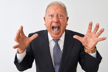 Senior grey-haired businessman wearing suit standing over isolated white background crazy and mad shouting and yelling with aggressive expression and arms raised. Frustration concept.