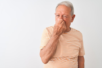 Senior grey-haired man wearing striped t-shirt standing over isolated white background smelling...