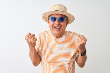 Naklejka premium Senior man wearing striped t-shirt sunglasses and sumer hat over isolated white background screaming proud and celebrating victory and success very excited, cheering emotion