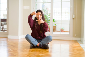 Young beautiful woman sitting on the floor at home smiling making frame with hands and fingers with happy face. Creativity and photography concept.