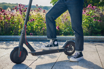 girl is taking her black and red electric scooter denim style flowers behind her outside