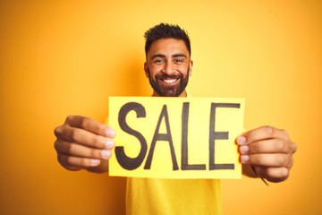 Young arab indian hispanic man holding sale banner over isolated yellow background with a happy face standing and smiling with a confident smile showing teeth
