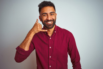 Fototapeta premium Young indian man wearing red elegant shirt standing over isolated grey background smiling doing phone gesture with hand and fingers like talking on the telephone. Communicating concepts.