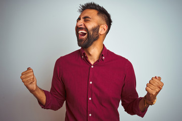 Young indian man wearing red elegant shirt standing over isolated grey background celebrating...