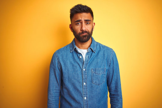 Young indian man wearing denim shirt standing over isolated yellow background depressed and worry for distress, crying angry and afraid. Sad expression.