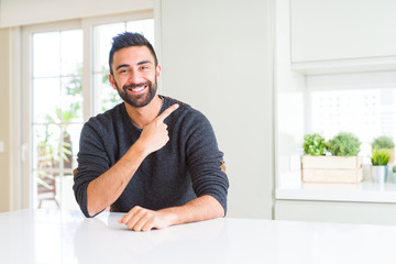 Handsome hispanic man wearing casual sweater at home cheerful with a smile of face pointing with hand and finger up to the side with happy and natural expression on face