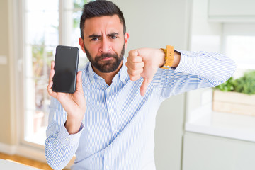 Handsome hispanic business man showing smartphone screen with angry face, negative sign showing dislike with thumbs down, rejection concept