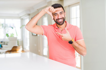 Handsome hispanic man wearing casual t-shirt at home smiling making frame with hands and fingers with happy face. Creativity and photography concept.