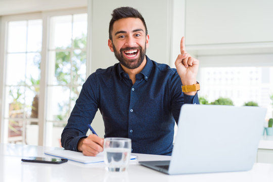Handsome hispanic man working using computer and writing on a paper surprised with an idea or question pointing finger with happy face, number one