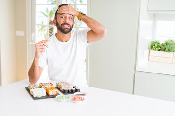 Handsome hispanic man eating asian sushi using chopsticks stressed with hand on head, shocked with shame and surprise face, angry and frustrated. Fear and upset for mistake.