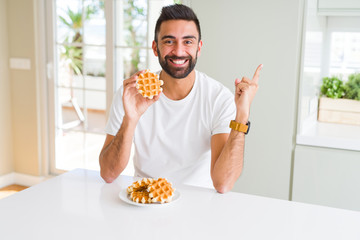 Handsome hispanic man eating sweet belgian waffle pastry very happy pointing with hand and finger to the side