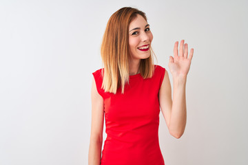 Redhead businesswoman wearing elegant red dress standing over isolated white background Waiving saying hello happy and smiling, friendly welcome gesture