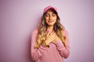 Young beautiful woman wearing cap over pink isolated background smiling with hands on chest with closed eyes and grateful gesture on face. Health concept.