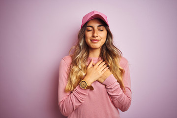 Naklejka premium Young beautiful woman wearing cap over pink isolated background smiling with hands on chest with closed eyes and grateful gesture on face. Health concept.