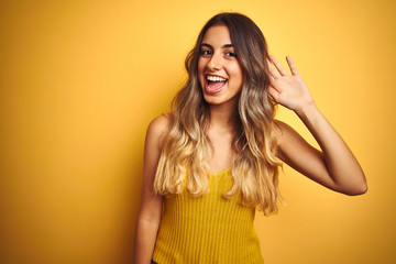 Fototapeta premium Young beautiful woman wearing t-shirt over yellow isolated background smiling with hand over ear listening an hearing to rumor or gossip. Deafness concept.