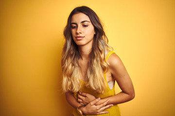 Young beautiful woman wearing t-shirt over yellow isolated background with hand on stomach because indigestion, painful illness feeling unwell. Ache concept.