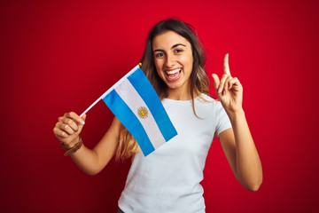 Young beautiful woman holding argentine flag over red isolated background surprised with an idea or question pointing finger with happy face, number one