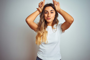 Fototapeta na wymiar Young beautiful woman wearing casual white t-shirt over isolated background doing funny gesture with finger over head as bull horns