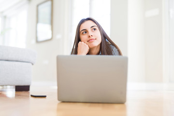 Beautiful young woman laying on the floor using laptop serious face thinking about question, very confused idea