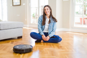 Young woman using automatic vacuum cleaner to clean the floor, controling machine housework robot