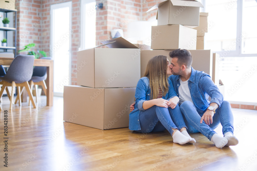 Wall mural young beautiful couple in love moving to new home, sitting on the floor very happy and cheerful for 