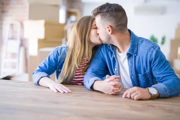 Young beautiful couple sitting on the table at home, hugging in love very happy for moving to new home with cardboard boxes behind them