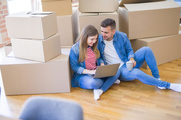 Young couple sitting on the floor around cardboard boxes using computer laptop, very happy moving to a new house