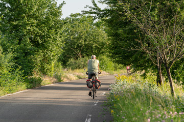 Fototapeta premium An unidentifiable man rides his bike on a road closed to cars between trees and meadows