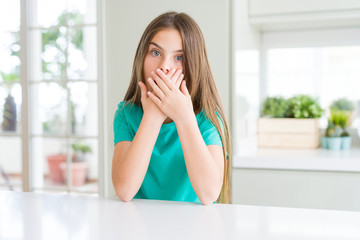 Beautiful young girl kid wearing green t-shirt shocked covering mouth with hands for mistake. Secret concept.