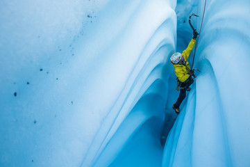 Narrow canyon of ice with wavy walls and an ice climber ascending the narrow slot.