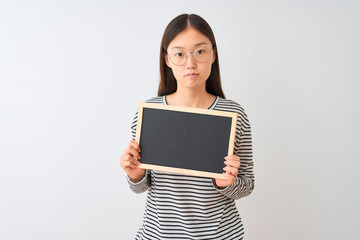 Young chinese woman wearing glasses holding blackboard over isolated white background with a confident expression on smart face thinking serious