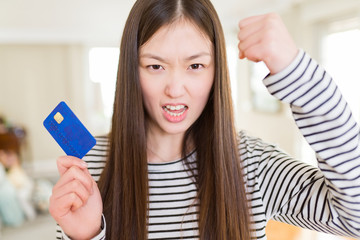 Beautiful Asian woman holding credit card annoyed and frustrated shouting with anger, crazy and yelling with raised hand, anger concept