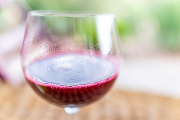 Macro closeup of glass of red pink purple wine or cranberry juice isolated with blurry background in garden