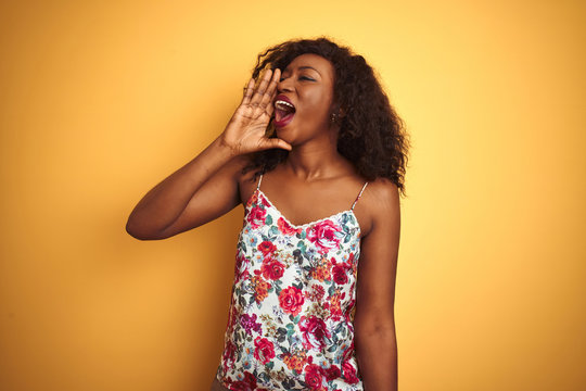 African american woman wearing floral summer t-shirt over isolated yellow background shouting and screaming loud to side with hand on mouth. Communication concept.