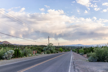 Colorful sunset on Bishops Lodge Road in Santa Fe, New Mexico with golden light, green plants and dirt road to residential community