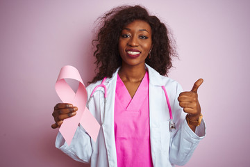 Young african american doctor woman holding cancer ribbon over isolated pink background happy with...